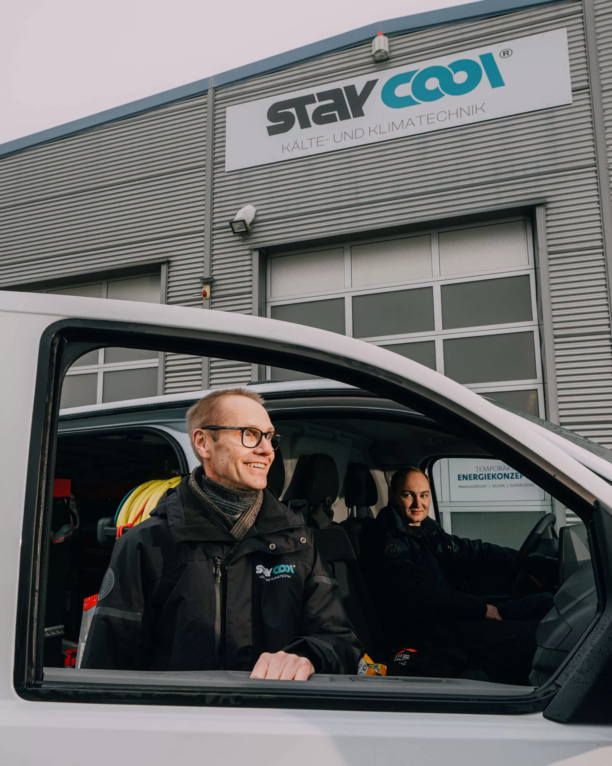 Zwei Mitarbeiter von Stay Cool in einem Firmenfahrzeug vor der Halle von Stay Cool Kältetechnik.
