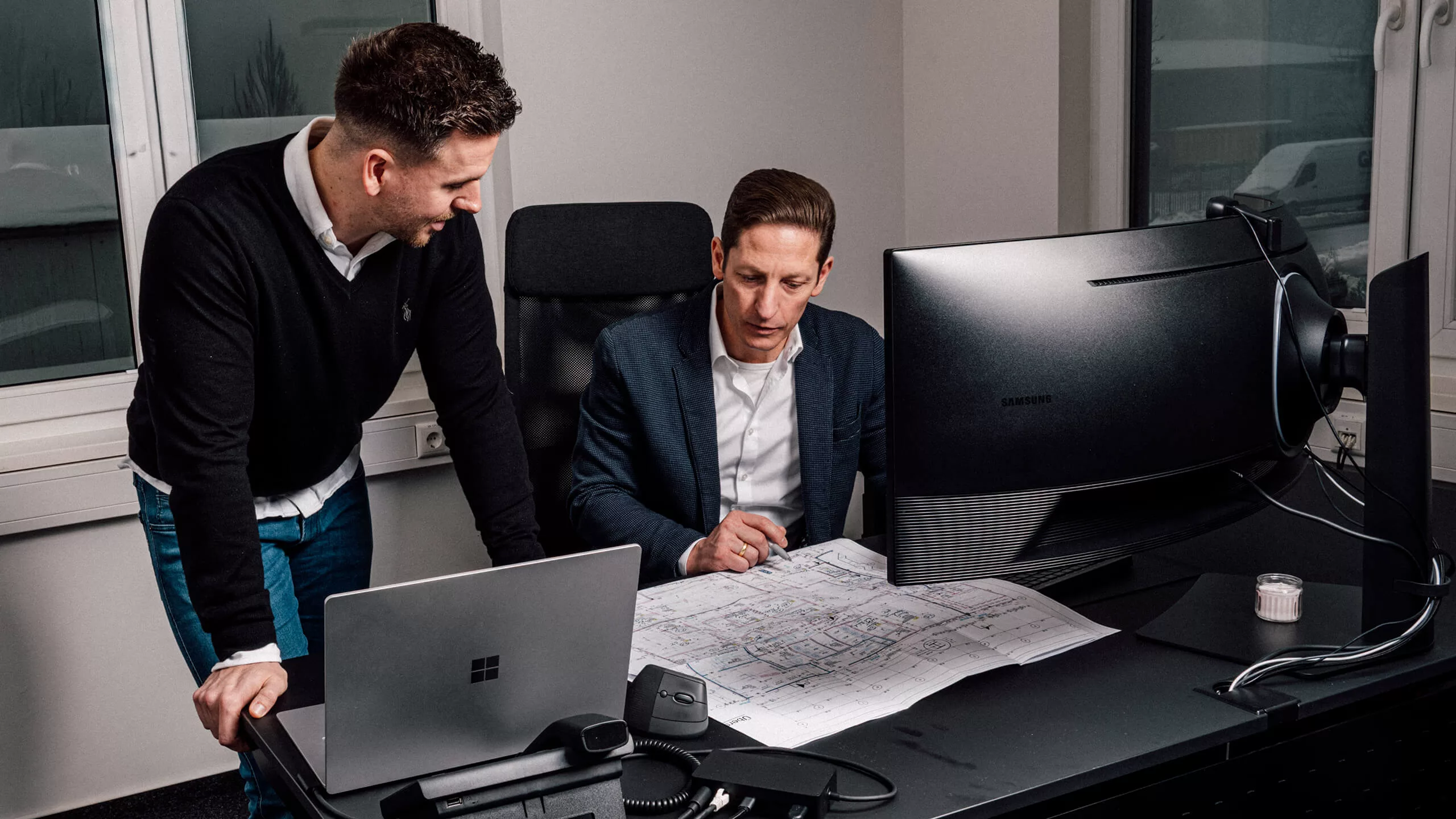 Ein Mitarbeiter und der Geschäftsführer der Kälte- und Klimatechnikfirma „Stay Cool” sitzen im Büro an einem Schreibtisch und führen eine Besprechung.