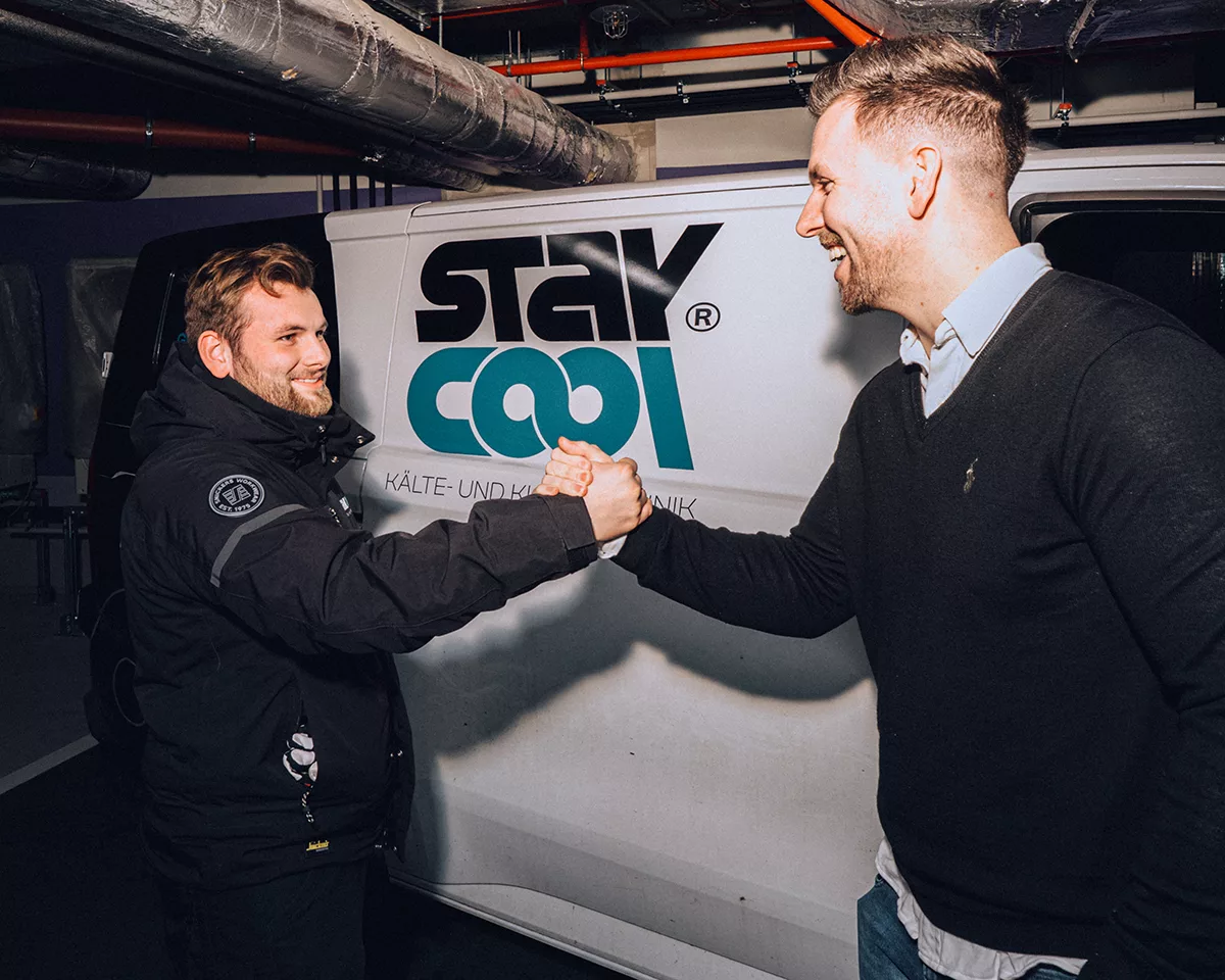 Mitarbeiter und Geschäftsführer von Stay Cool stehen vor einem Firmentransporter und klatschen sich lächelnd in die Hände.